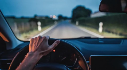 Silhouette d'un conducteur au volant, main posée sur la ceinture de sécurité, symbolisant la protection corporelle vitale de l'assurance auto