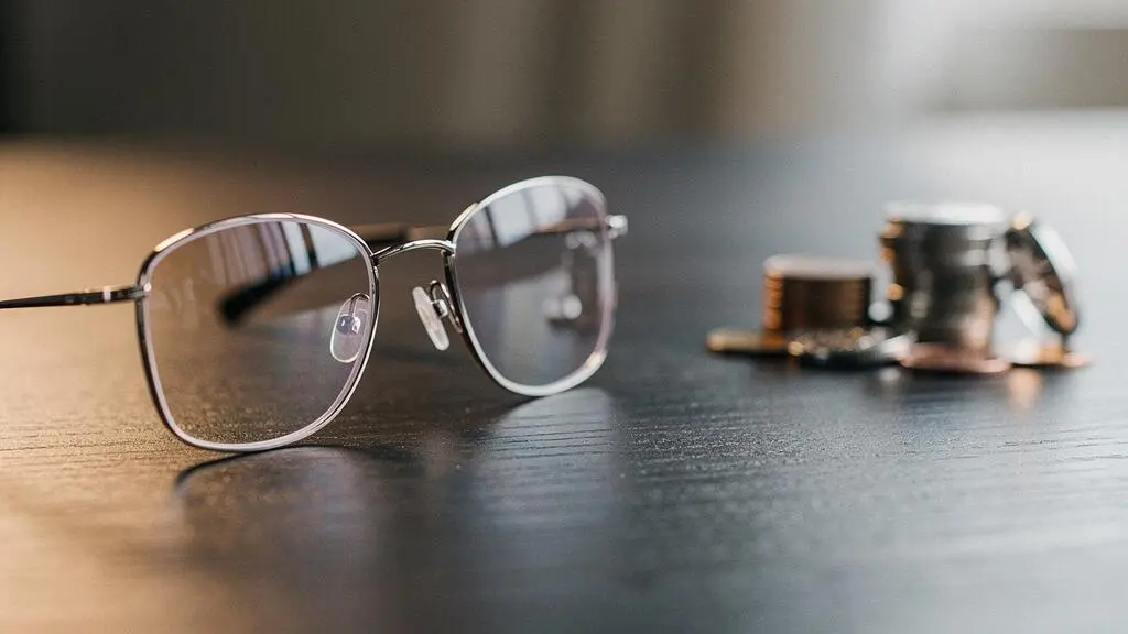 Paire de lunettes à verres progressifs posée sur une table en bois avec une lumière douce évoquant le coût caché de l'équipement optique